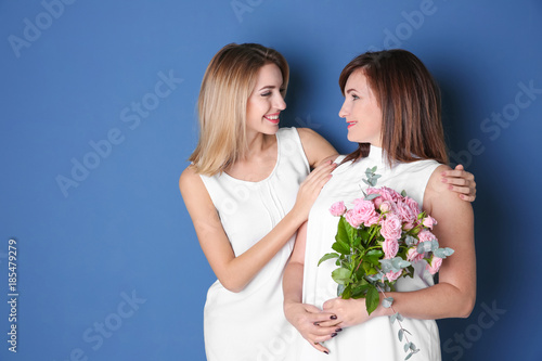 Attractive young woman with her mother in matching dresses on color background
