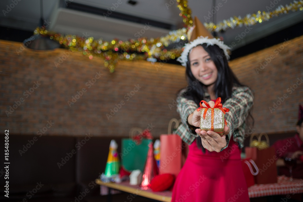beautiful woman wear red dress and santa claus hat showing golden gift box on hand  in restaurant. concept of Christmas party and New year party with copy space for text.