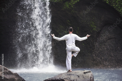 Man standing in meditation yoga on rock at waterfall