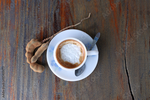 Cappuccino coffee in the white cup with coffee spoon and tamarind on the wooden table.