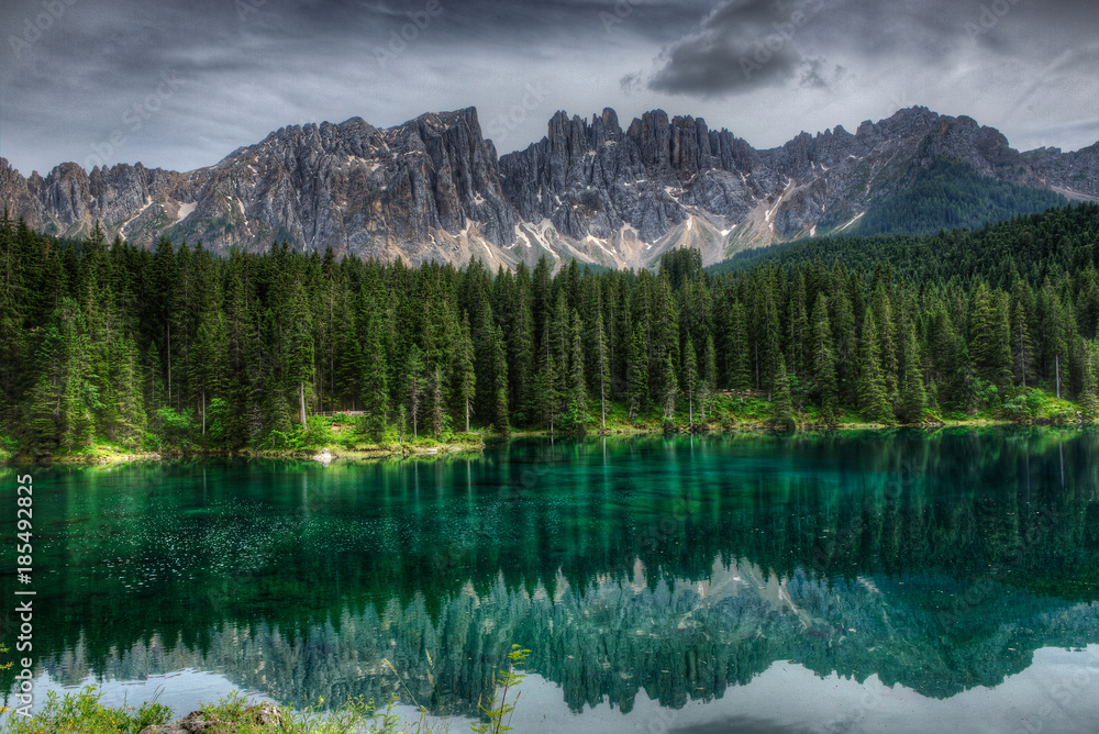 Green lake with reflection of forrest and alpine mountains
