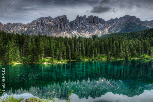 Green lake with reflection of forrest and alpine mountains