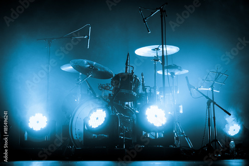 A kit of drums and a microphones on an empty stage in blue smoke before the concert