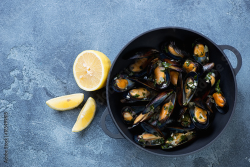 Above view of a cast-iron pan with freshly cooked mussels, blue stone background with copyspace, horizontal shot