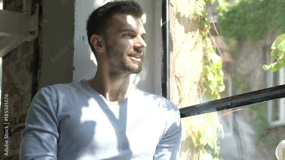 Handsome man in blue sweater sitting on window's sill and looks happy, steadycam shot
Handsome man in blue sweater sitting on window's sill and looks happy, steadycam shot
