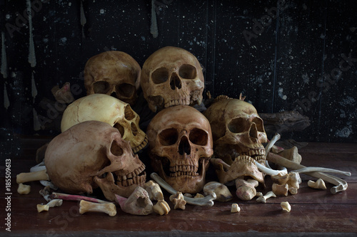 Pile of skulls and bone put on the wooden table which has dirty wall in dim light room