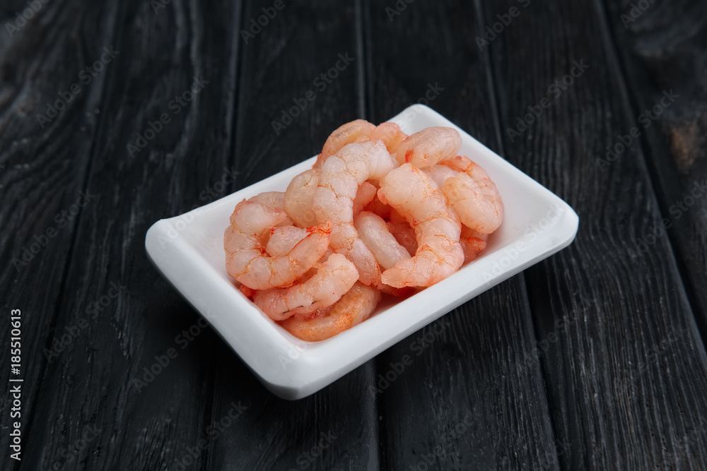 Small boiled peeled shrimps in small plate on dark wooden background Small boiled peeled shrimps in small plate on dark wooden background