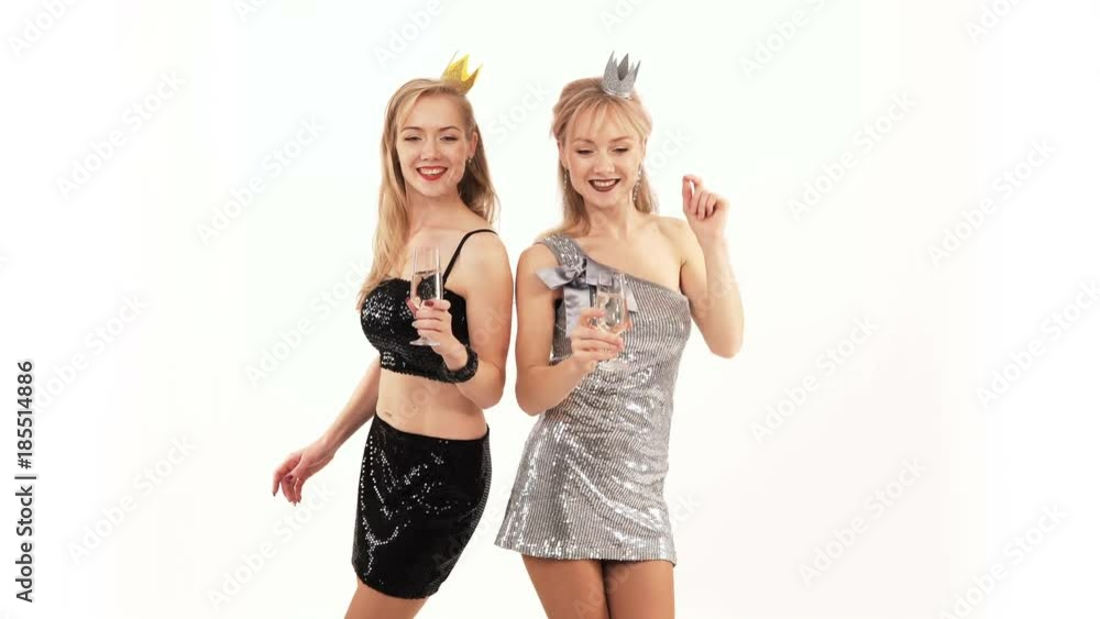 2 beautiful cheerful twin girls with glasses of champagne dancing in the studio on a white background 2 beautiful cheerful twin girls with glasses of champagne dancing in the studio on a white background