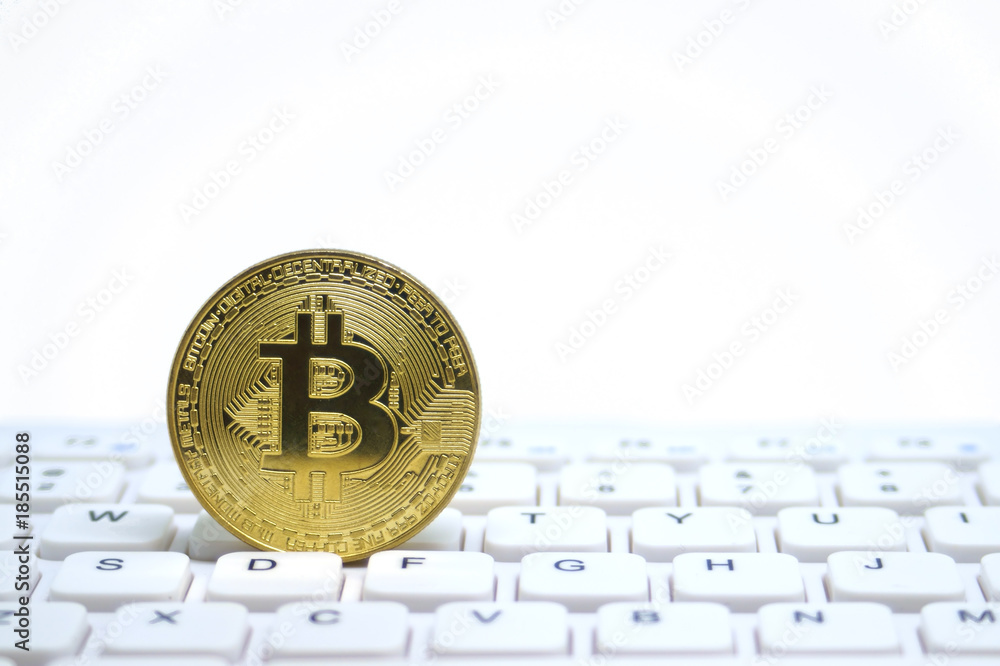 Golden symbolic coin of bitcoin on white keyboard.