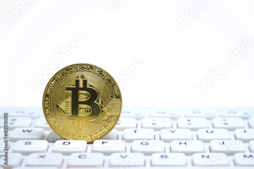Golden symbolic coin of bitcoin on white keyboard.