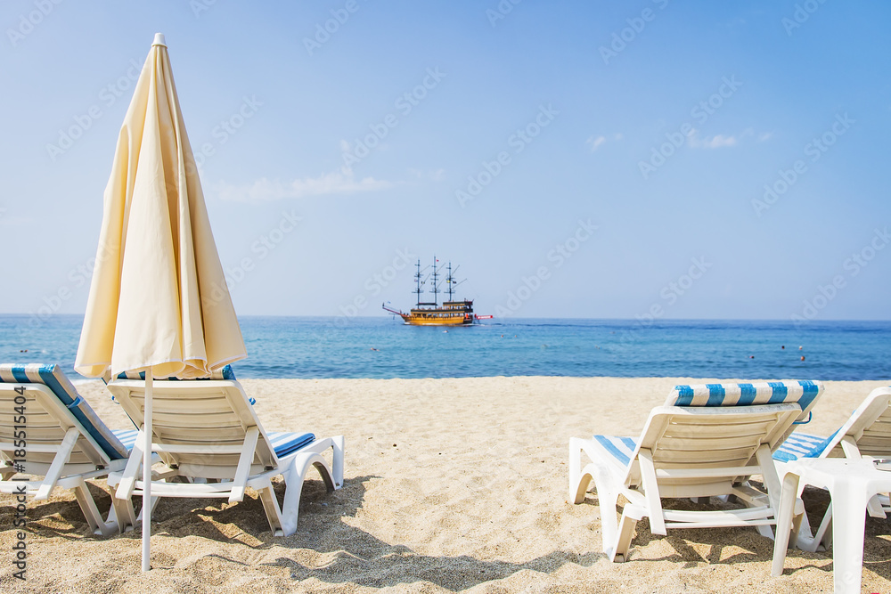 Sunbeds and sun umbrellas on white sand of tropical beach on blue sea background in bright sunny summer day. Summer vacation at beach resorts
