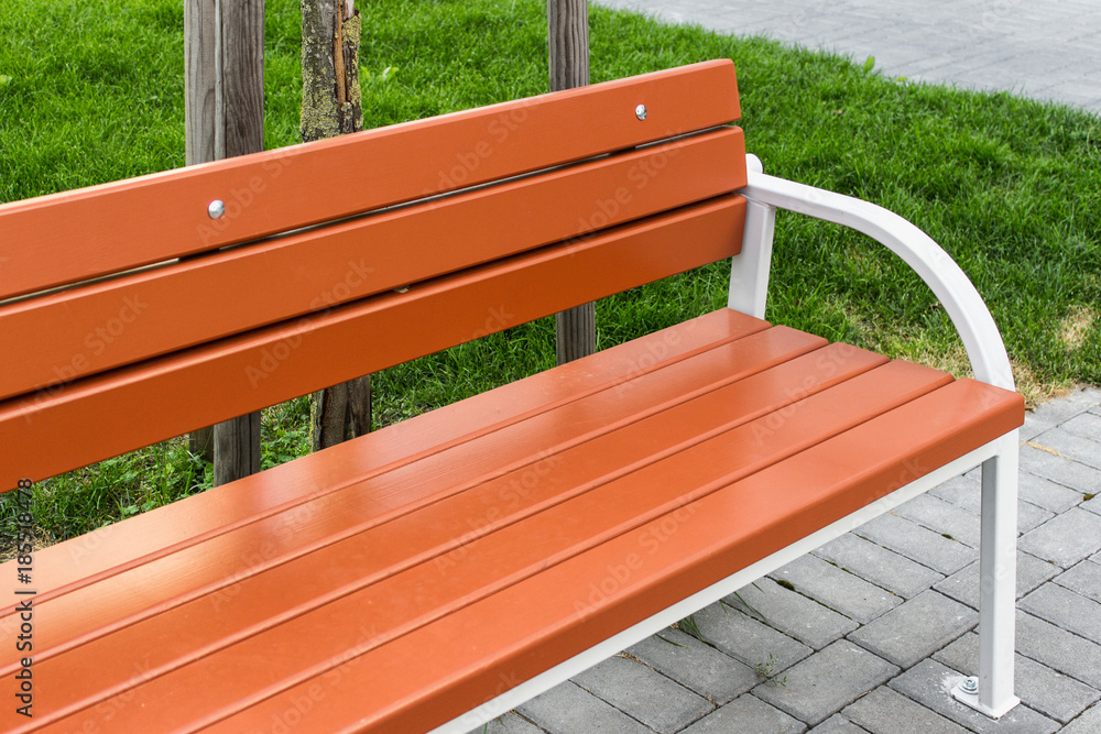 Freshly painted orange park bench. City and public park infrastructure.  Outdoor details. Photos | Adobe Stock