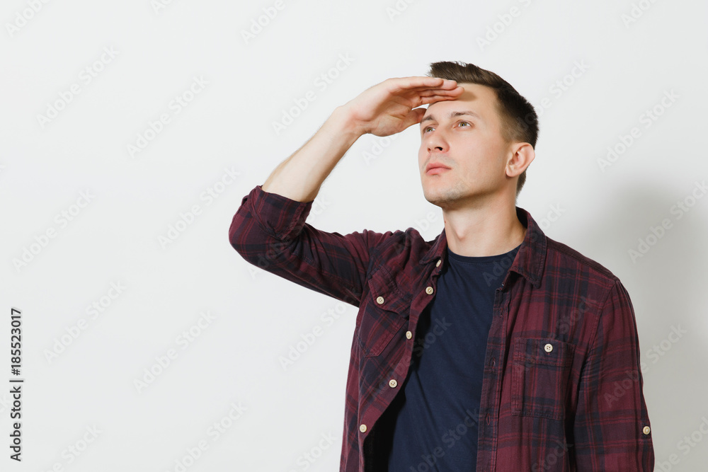 Portrait of handsome serious caucasian young in plaid red shirt holding his hand at forehead looking far away isolated on white background. Copy space for advertisement. With place for text. Portrait of handsome serious caucasian young in plaid red shirt holding his hand at forehead looking far away isolated on white background. Copy space for advertisement. With place for text.