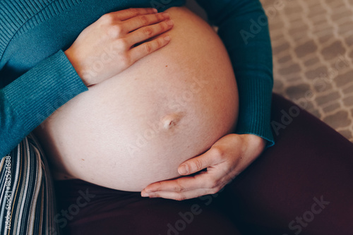 young pregnant woman resting on a sofa, holding her growing baby belly gently. concept for pregnancy, relaxation and the joy of expecting a child. beautiful belly skin, no strech marks.