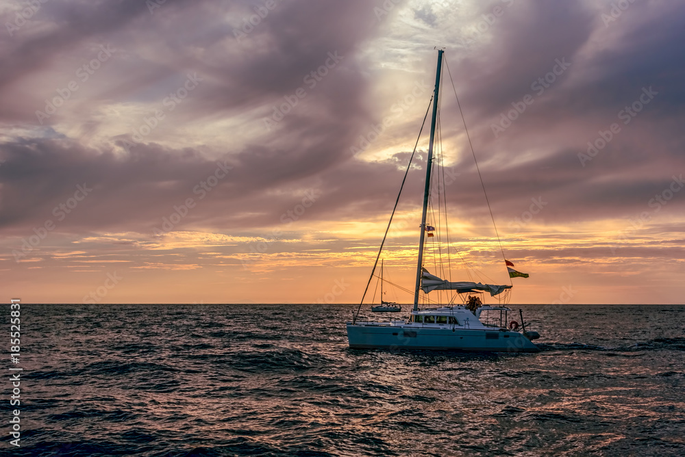 Sailboat on open sea during sunset under cloudy skies