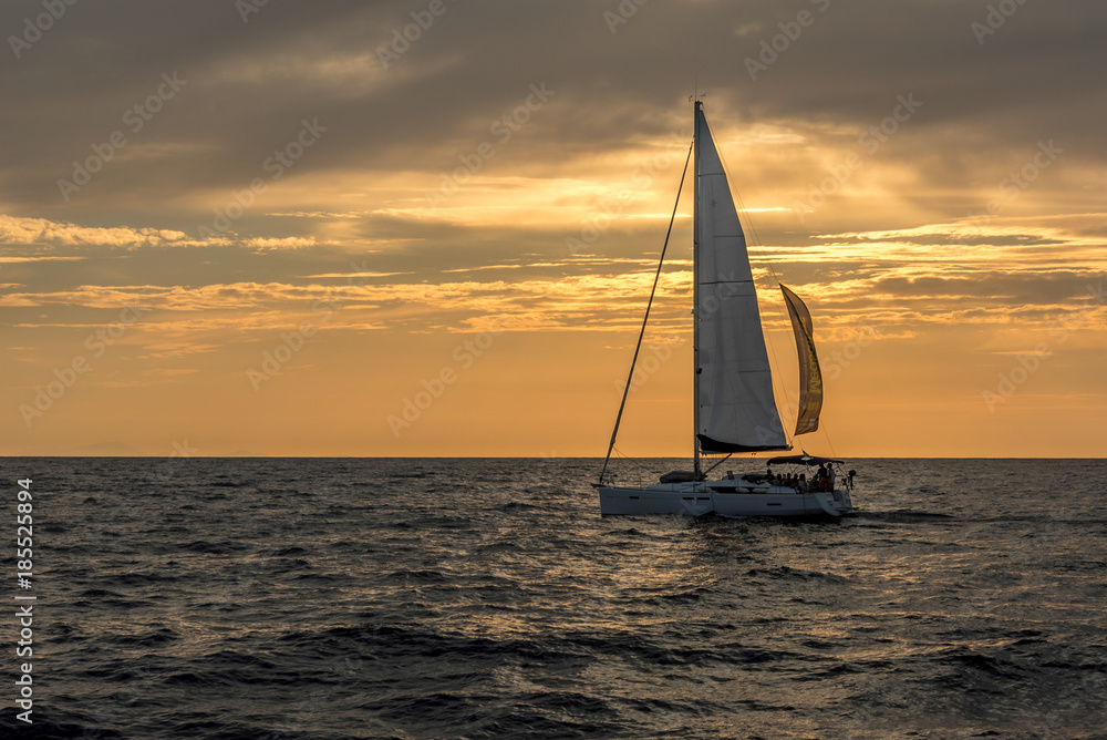 Sailboat on open sea during sunset under cloudy skies