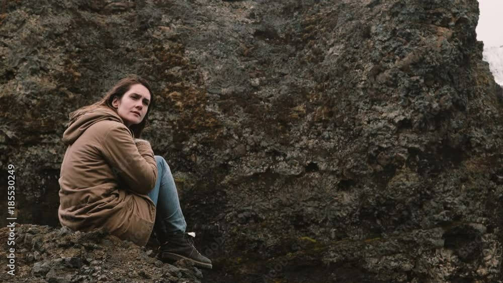 Young beautiful woman sitting on the rock in mountains and thinking alone. Tourist resting after hiking in Iceland. Young beautiful woman sitting on the rock in mountains and thinking alone. Tourist resting after hiking in Iceland.