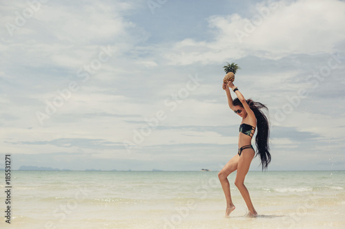 Beautiful happy female with very long hair holding pineapples on sea shore