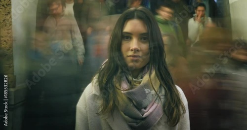 Beautiful young woman standing in moving crowd in subway, looking at camera