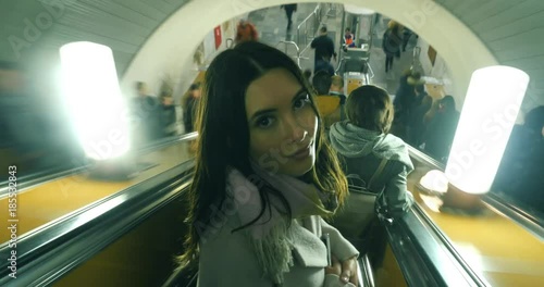 Beautiful young woman in crowded city, standing on subway escalator moving down,