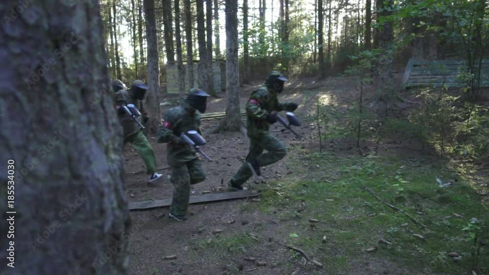 Paintball player running on battle field during shooting game in summer forest slow motion. Team