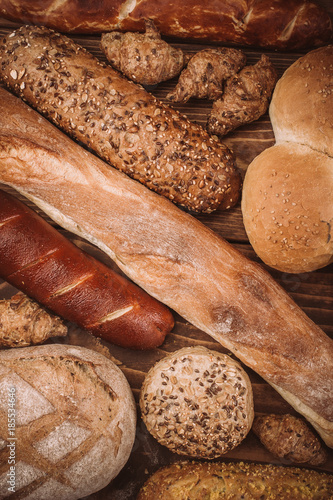 Many mixed baked breads and rolls on rustic wooden table