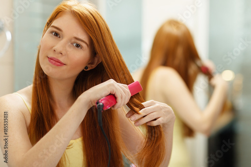 Beautiful Woman Ironing Healthy Red Hair With Iron Straightener