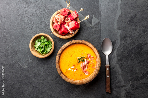 Salmorejo soup with watermelon. Traditional spanish cold tomato soup with watermelon and ham serrano in olive wooden bowl, slate background, top view