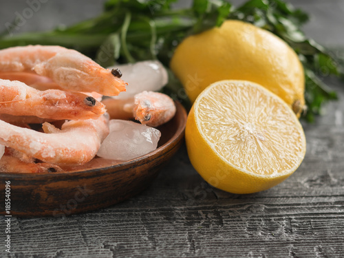 Frozen shrimp with lemon and herbs on clay bowl on black wooden rustic table.