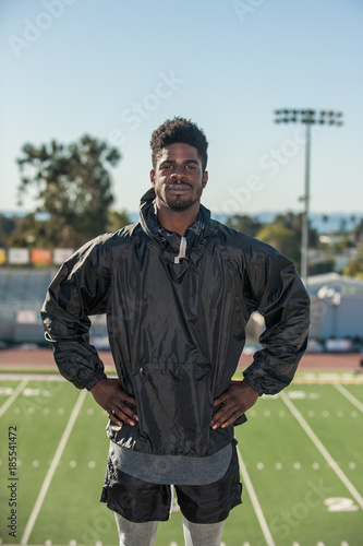 Lean Jamaican athlete in heroic hands on hips pose overlooking stadium. 