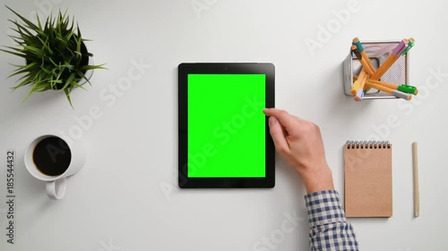 A man's finger scrolling on the green touchscreen. A tablet is on the white table. View from the top. Close-up.