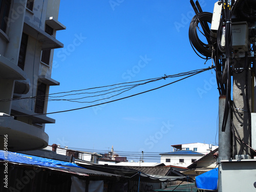 Clear blue gradient winter sky with old style building and messy electrical pole on both sides, and small house roof, dirty aluminum corrugated wall with plastic canvas shade, power line cord crossing