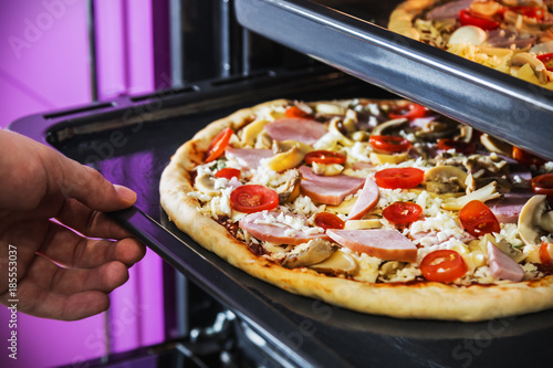 hand moves the tray of pizza with mushrooms, ham and mozzarella cooked baking in the oven