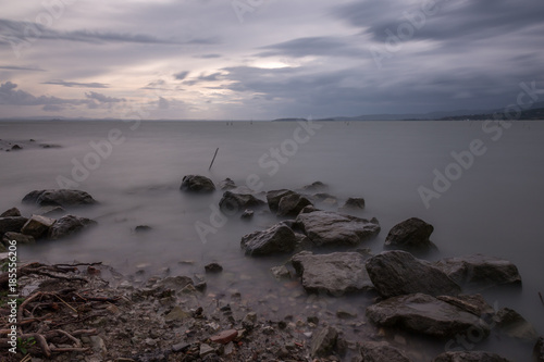 A minimalist, long exposure photo of some big rocks in Trasimeno lake (Umbria), with perfectly still water and cloudy sky
