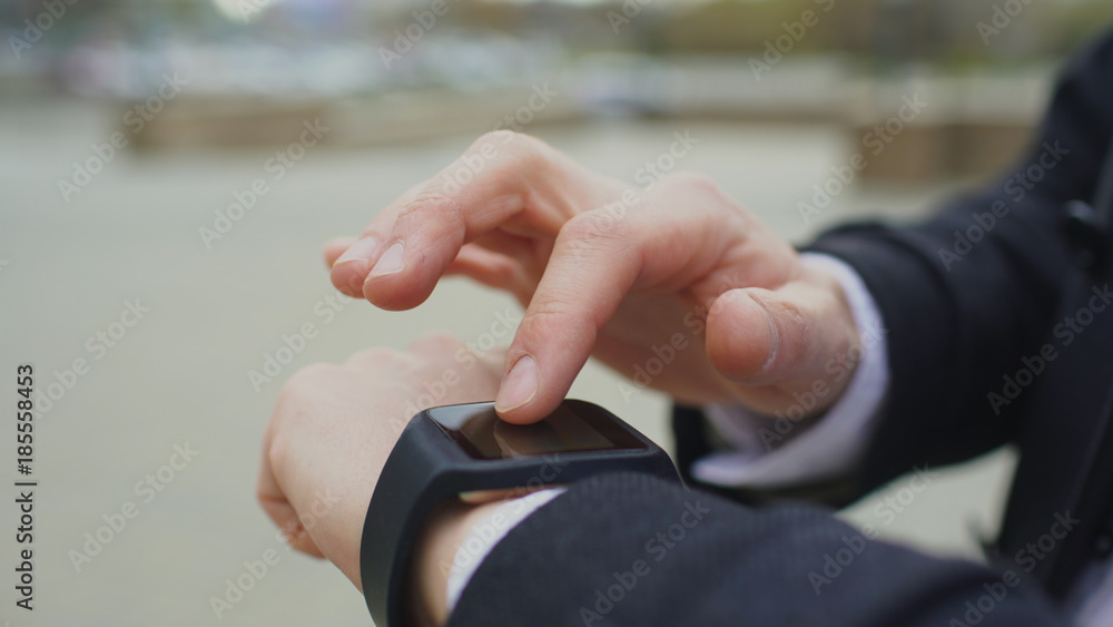 Closeup of businessman hand using his smartwatch touchscreen standing on the street