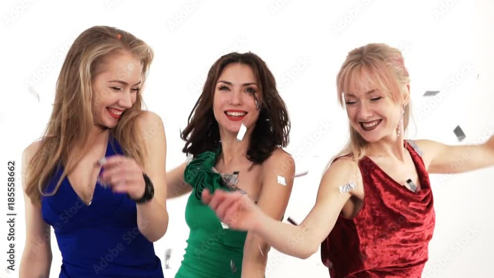3 beautiful girls in bright dresses throwing confetti at a party in a studio on a white background 3 beautiful girls in bright dresses throwing confetti at a party in a studio on a white background