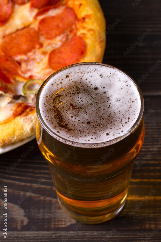 Beer and pizza on dark wooden background. Ale and food. View from above, top, vertical