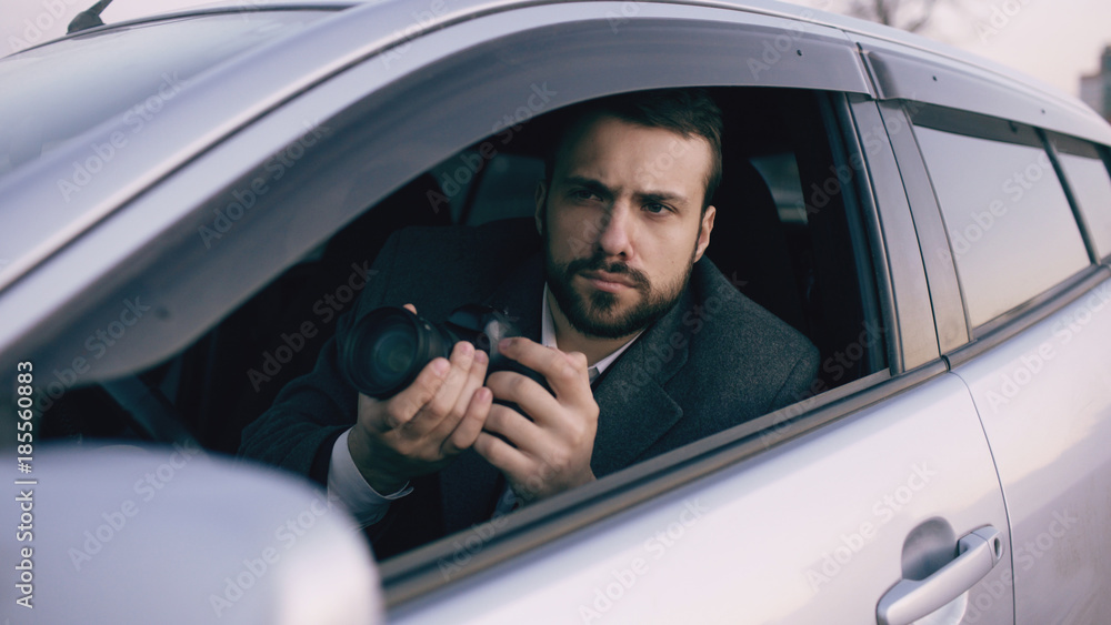 Young private detective man sitting inside car and photographing with dslr camera Young private detective man sitting inside car and photographing with dslr camera