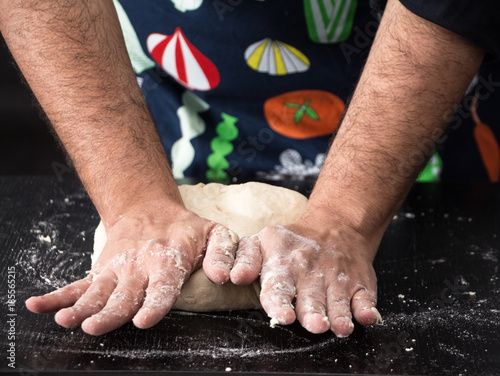 Male hands kneading dough, baking preparation closeup. © okolaa