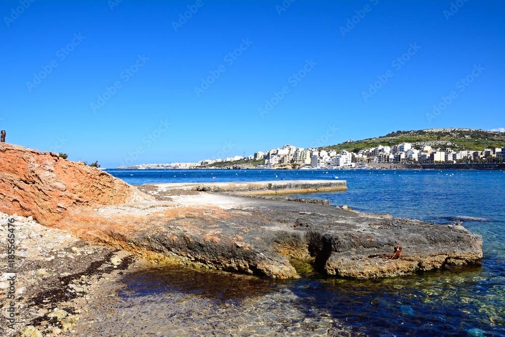 Rocky shoreline with views across the bay towards St Pauls Bay,  Xenxija Bay, Malta.