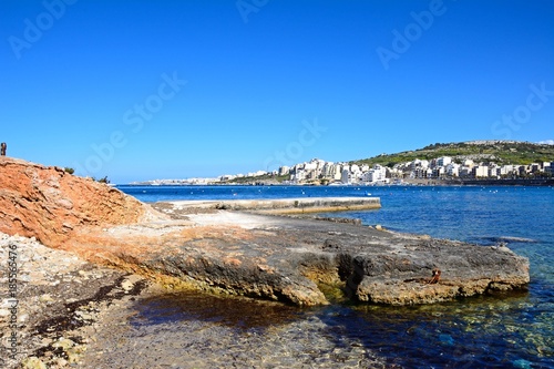 Rocky shoreline with views across the bay towards St Pauls Bay, Xenxija Bay, Malta.