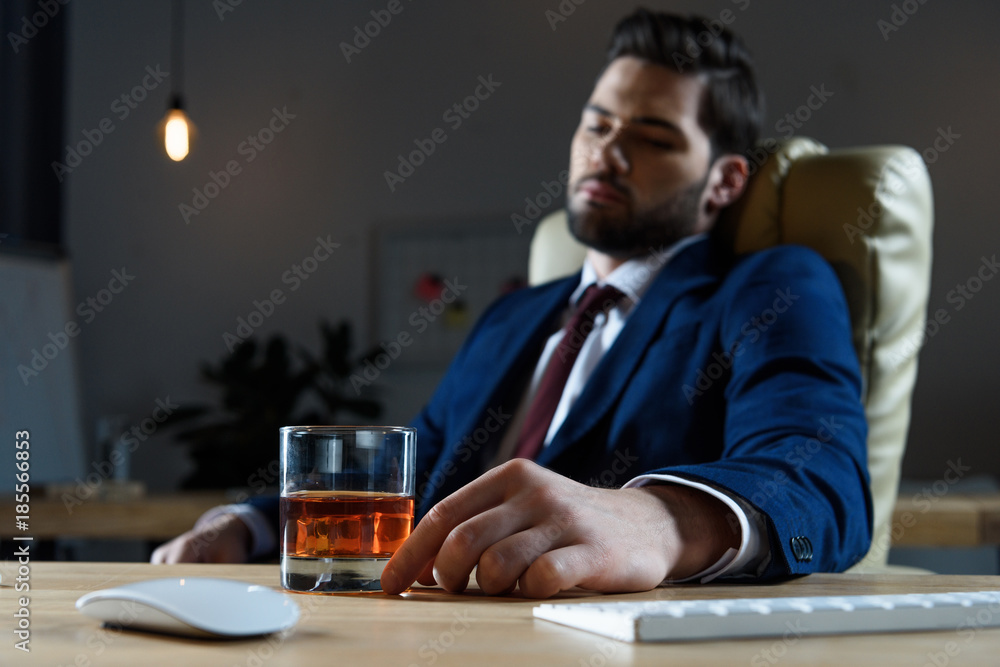 tired businessman sitting in chair and looking at glass of whiskey tired businessman sitting in chair and looking at glass of whiskey