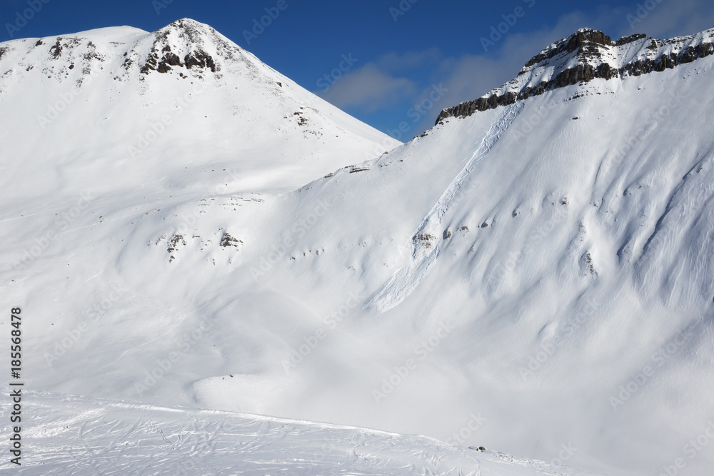 Snowy off-piste slope with traces of skis, snowboards and avalanches