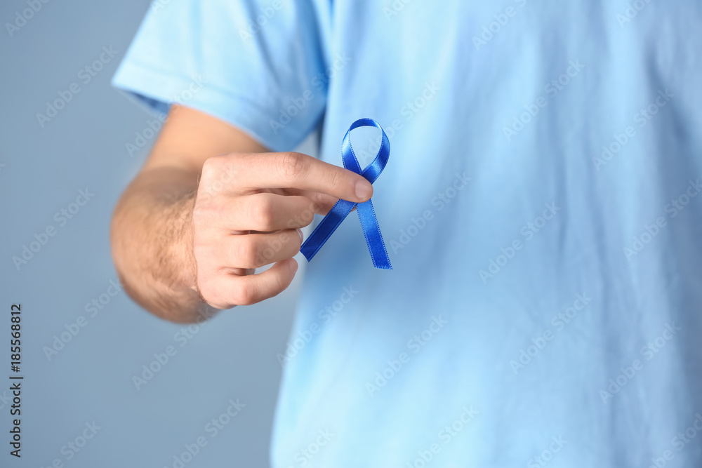 Young man holding blue ribbon on color background, closeup. Prostate cancer awareness concept Young man holding blue ribbon on color background, closeup. Prostate cancer awareness concept