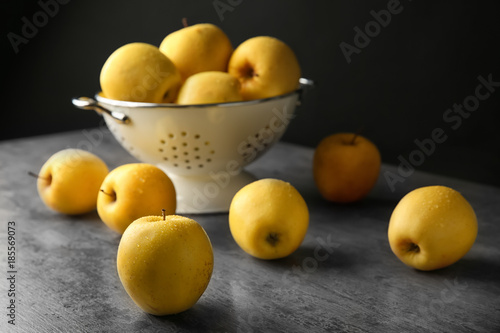 Ripe yellow apples near colander on table