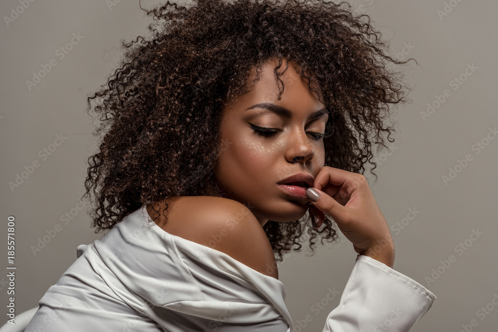 Attractive young african american woman in white shirt touching lips isolated on grey background