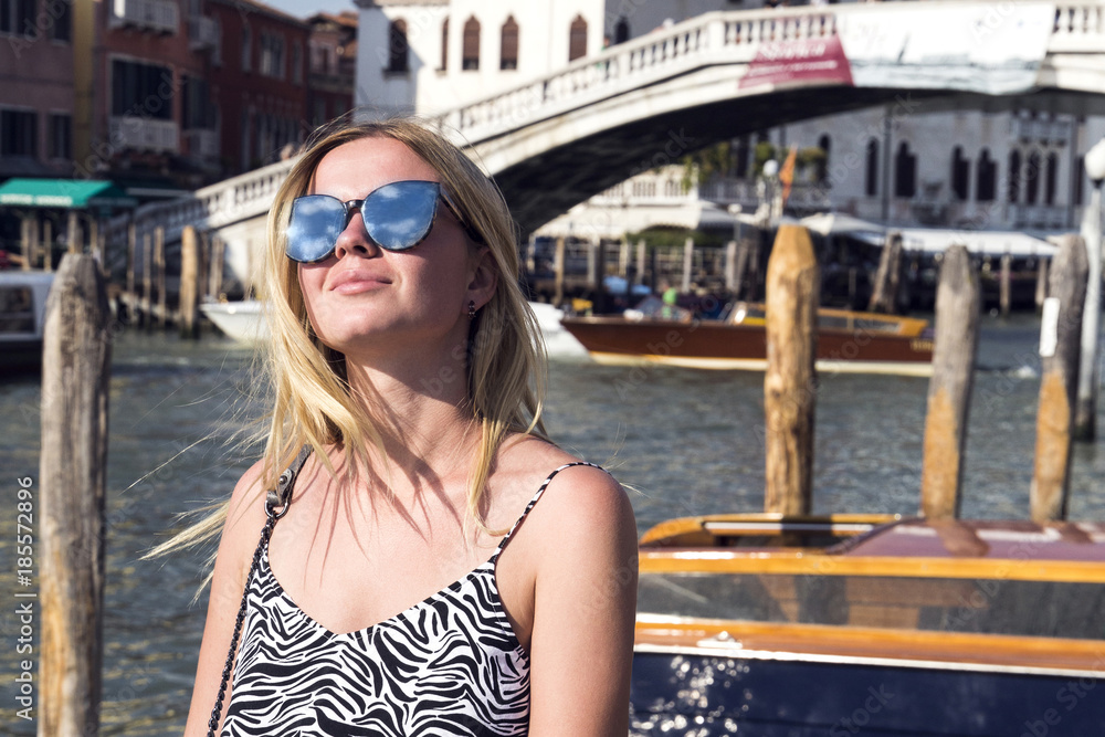 A beautiful girl in sunglasses which reflects the sky against the background of one of the bridges in Venice A beautiful girl in sunglasses which reflects the sky against the background of one of the bridges in Venice