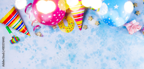 Bright colorful carnival or party border of balloons, streamers and confetti on blue table. Flat lay style, birthday or party greeting card with copy space and bokeh lights
