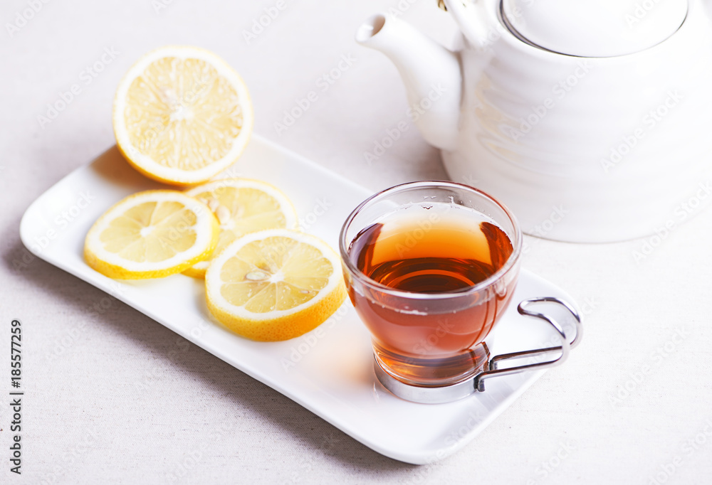 Tea cup with lemon on white plate next to teapot. Infusion. Tea cup with lemon on white plate next to teapot. Infusion.