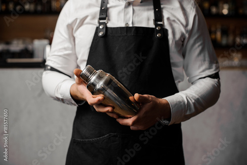 Barmans hands holding a shaker against the bar counter